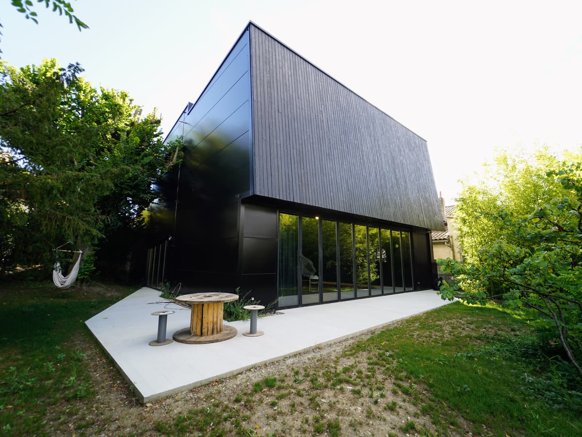 La Fabrique, volume de bois noir posé au fond du jardin, et sa terrasse